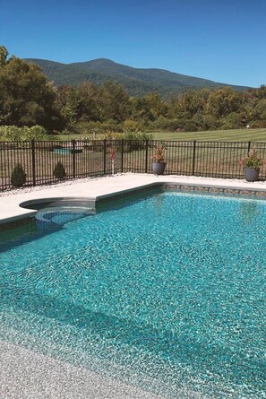 Una piscina con agua cristalina, rodeada por una valla negra, y una montaña al fondo.