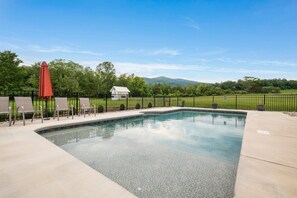 A rectangular swimming pool with a clear blue sky and mountains in the background.
