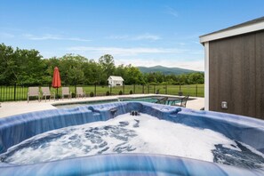 Un jacuzzi con vistas a una casa y montañas al fondo.