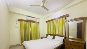 A bedroom with a bed, a ceiling fan, an air conditioning unit, a mirror, and a window with curtains.