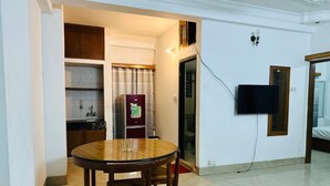 A compact living space with a dining area, kitchenette, and a TV mounted on the wall.