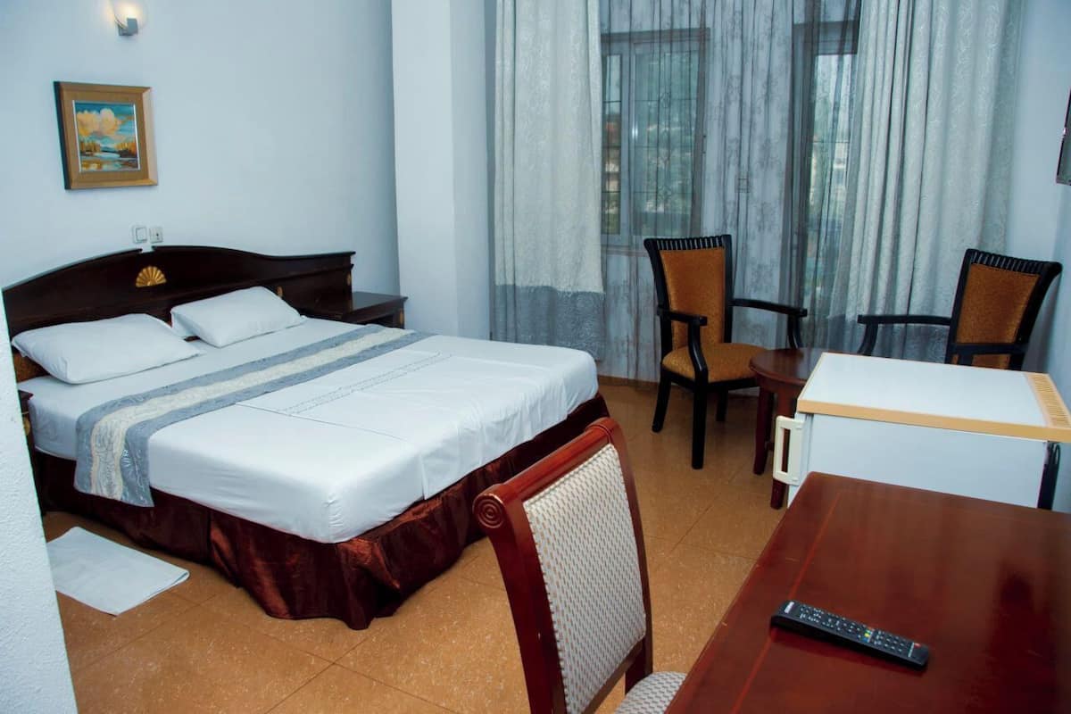 Quarto de hotel com cama, duas cadeiras, uma mesinha e controle remoto.