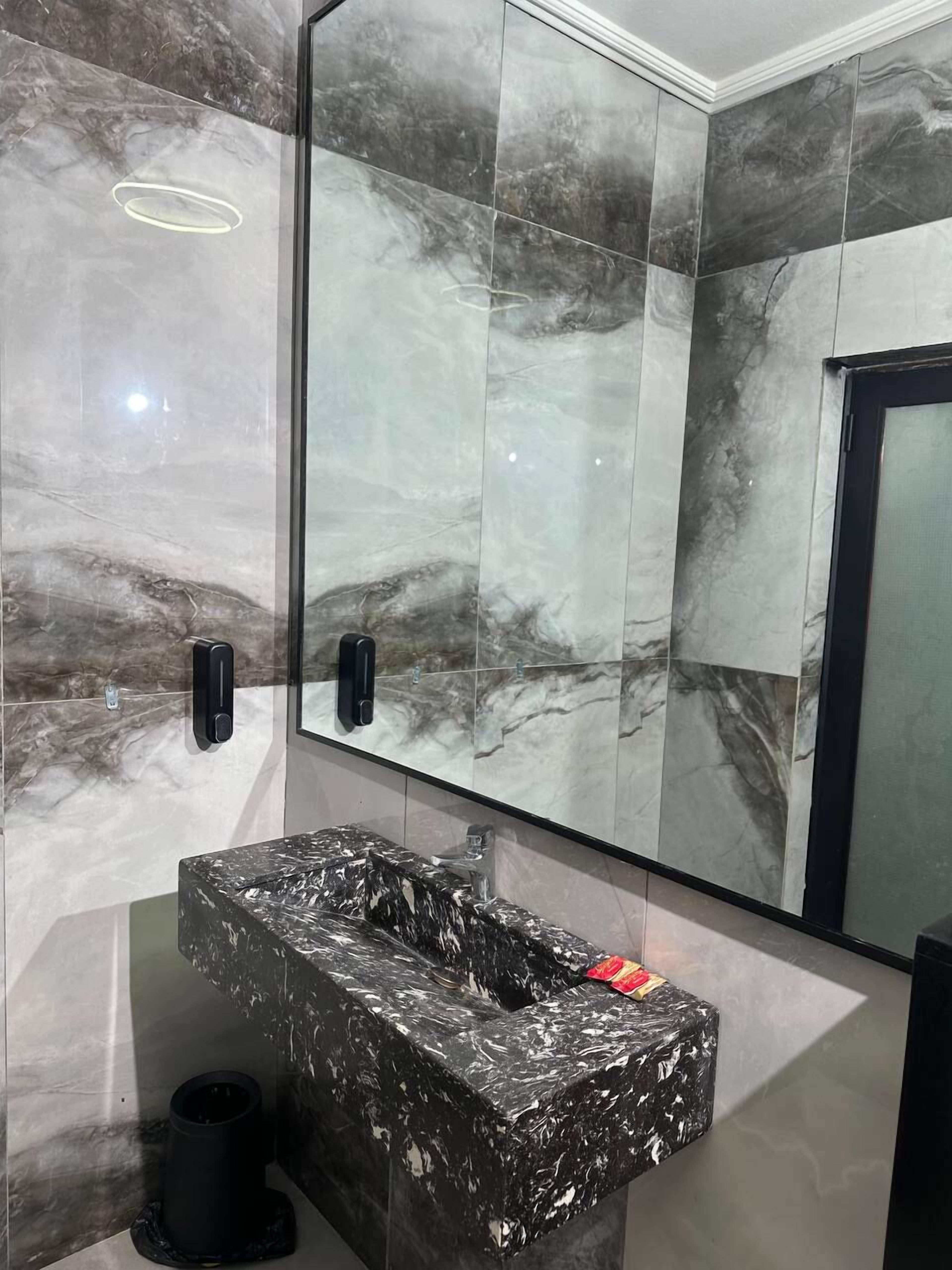 A modern bathroom with a marble vanity, a large mirror, and a handheld showerhead.