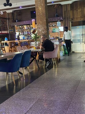 Un restaurante con barra, asientos con sillas azules y una persona caminando al fondo.