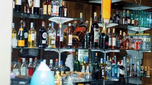 Een bar met meerdere planken vol met diverse flessen alcohol, waaronder sterke drank, wijn en bier.