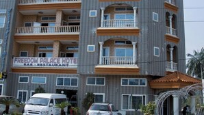 Een meerlaags hotel met balkons, een bar-restaurant en een parkeerplaats met voertuigen.