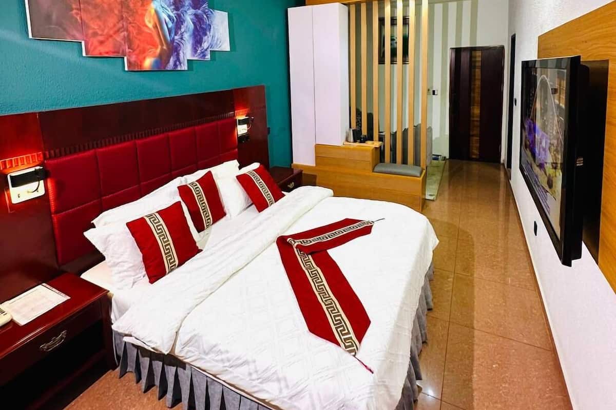 Quarto de hotel com uma cama grande, cabeceira vermelha, parede de destaque verde-água e banheiro moderno visível através de uma porta aberta.
