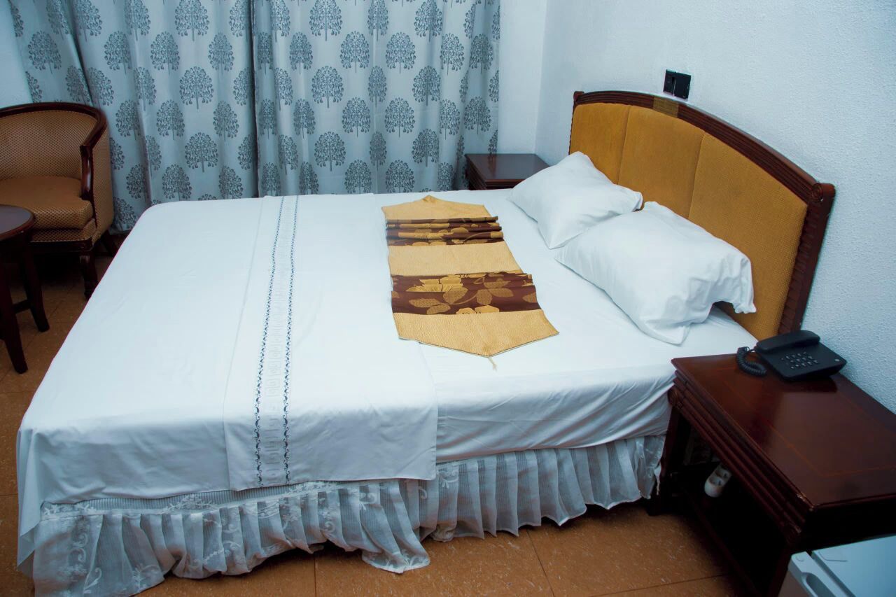 A neatly made bed with a white bedspread, a decorative throw, and a wooden headboard. There is a wooden nightstand with a telephone beside the bed.