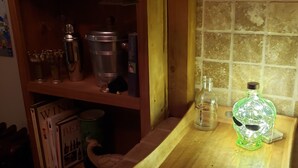 Een keuken met een houten plank met verschillende keukenspullen, een aanrecht met een groene fles en een betegelde spatwand.