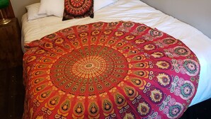 Een bed met een rode en gouden parelmoerprint deken, witte kussens en twee ingelijste posters aan de muur.