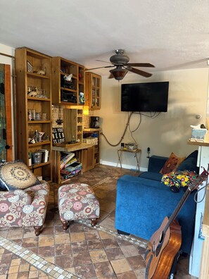 A living room with a blue sofa, patterned ottomans, a wooden bookshelf, a television, and a guitar. - Funky musical cottage near Lake Michigan PET Friendly!!! (Norton Shores)