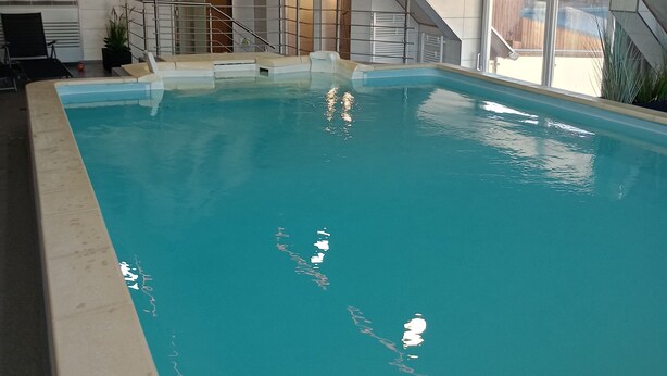 Una piscina interior con techo inclinado, agua cristalina y un mural de cascada en la pared.