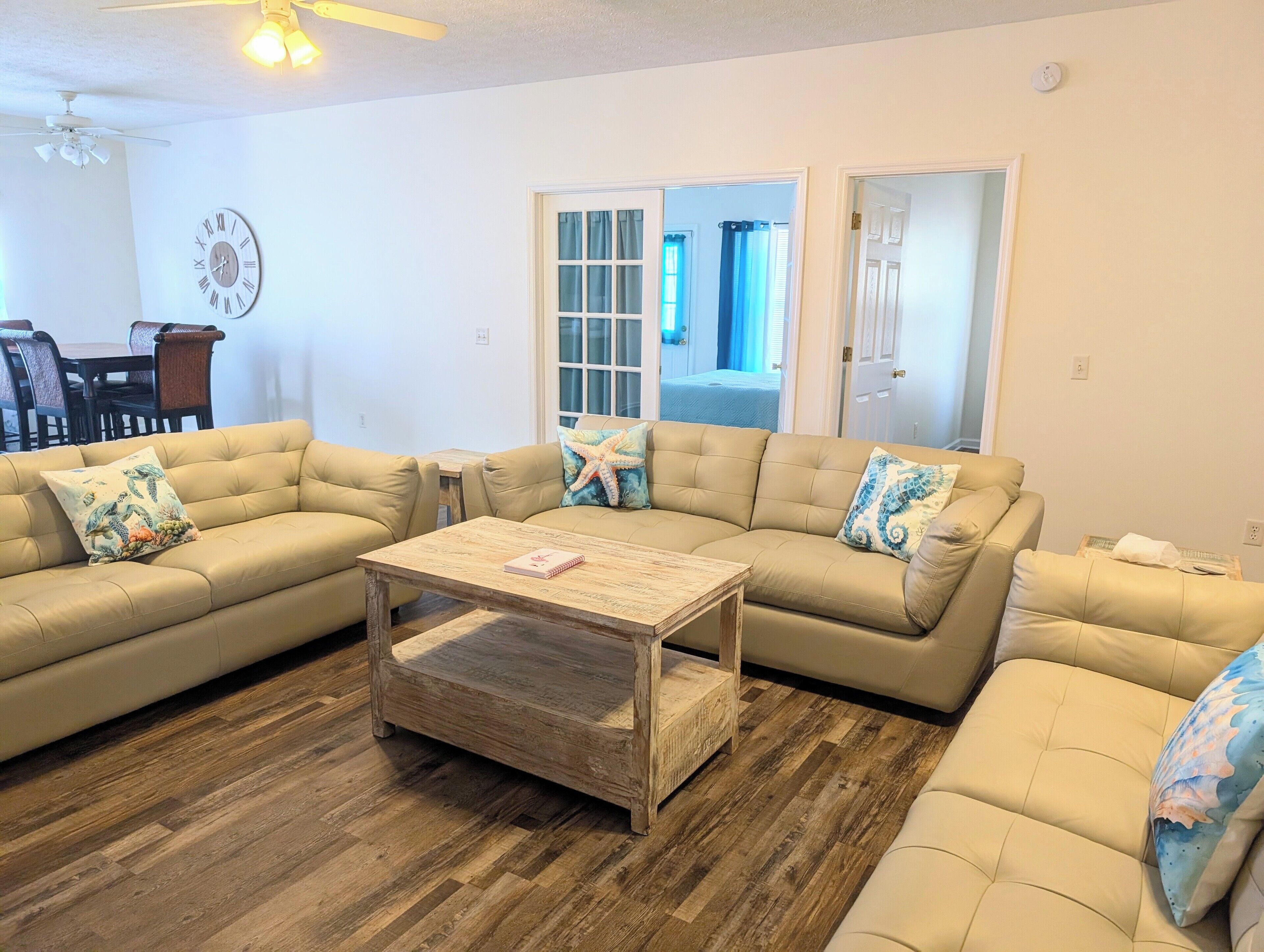 A living room with two beige sofas, a wooden coffee table, and a wall clock.