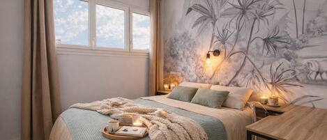 A bedroom with a bed, bedside tables, a nightstand, a window, and a wall mural.