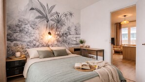 A bedroom with a bed, a desk, and a mural of tropical scenery.