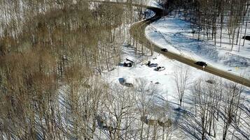 A snow-covered landscape with a winding road, sparse trees, and parked vehicles.