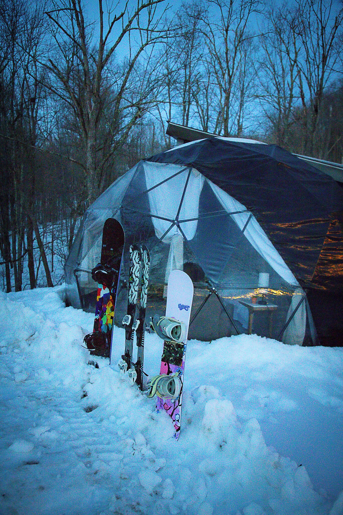 A geodesic dome structure in a snowy outdoor setting with snowboards leaning against it.