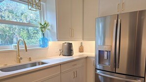 A modern kitchen with white cabinets, stainless steel appliances, and a window with a view of greenery.