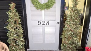 A front door with a wreath, number 928, and two potted plants on either side.
