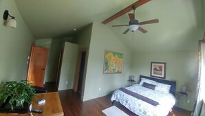A bedroom with a bed, ceiling fan, artwork, and a plant. -  Hemlock Room (Gabriola)