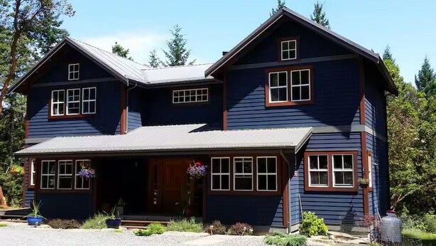A two-story house with a front porch, multiple windows, and a gravel driveway. -  Hemlock Room (Gabriola)