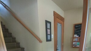 A staircase with carpeted steps leading to a door with a frosted glass panel. A wooden handrail is on the left, and a bulletin board with notes is on the wall to the right. -  Hemlock Room (Gabriola)