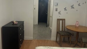 A bedroom with a bed, a dresser, a chair, a table, and a ceiling light fixture.