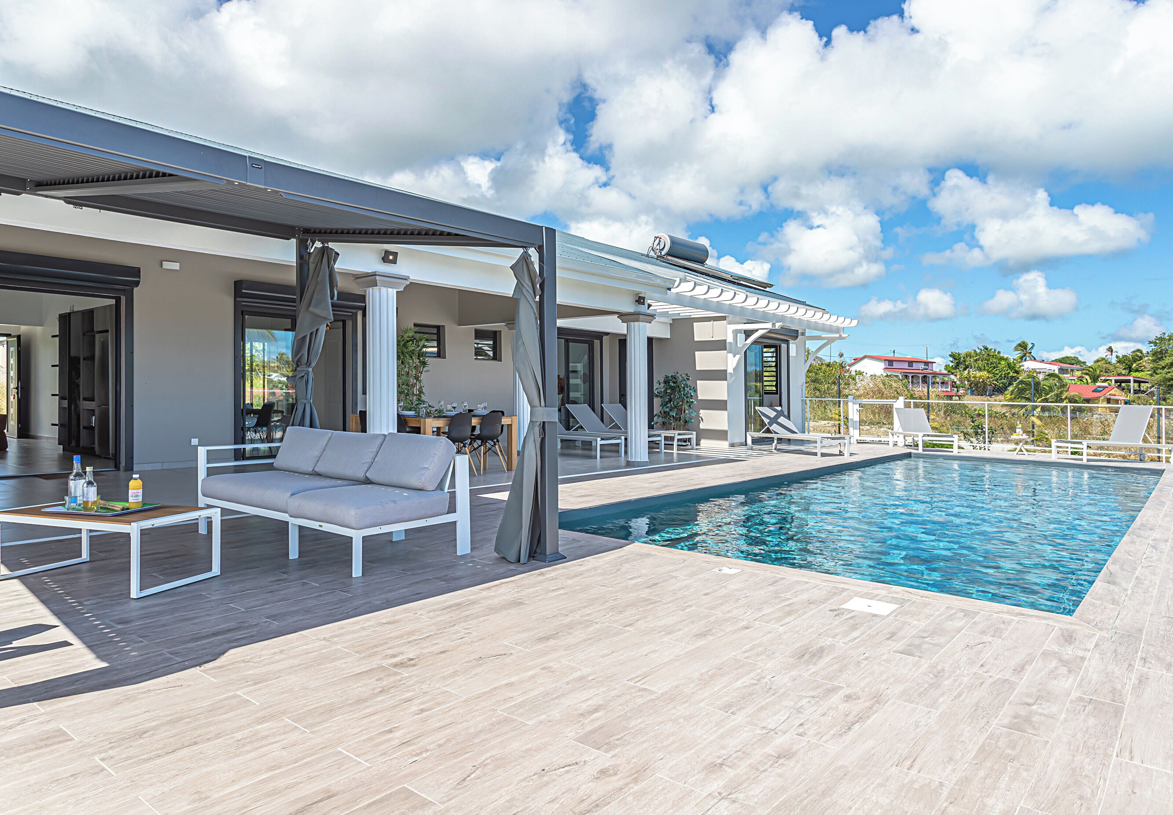 A modern outdoor pool area with a covered seating area, a dining setup, and a clear view of the surrounding landscape.