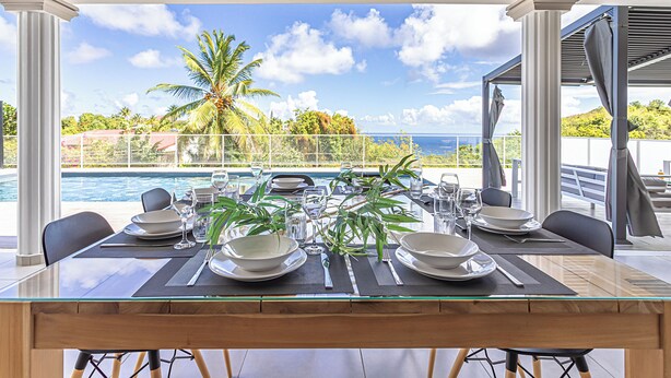 Mesa de comedor para cuatro con vista a una piscina y palmeras.