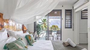 Habitación de hotel con cama, balcón y vista a palmeras, además de una puerta corrediza de vidrio.