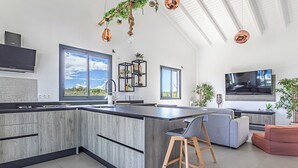 Cocina moderna con una isla grande, electrodomésticos integrados y zona de comedor con sofá y taburetes de bar.
