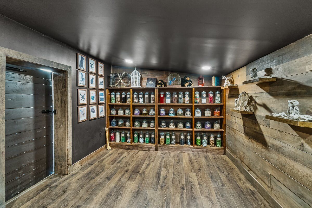 A room with wooden flooring, a wall of framed pictures, and shelves with jars and decorative items.