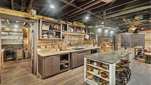 Eine rustikale Küche mit Holzböden, einer zentralen Kochinsel mit Hockern und Regalen mit Geschirr und Küchenutensilien.
