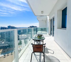Enjoy the city view from this balcony with a glass railing, small table, and chair.