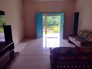 A room with a sofa, a TV, and a door leading to an outdoor area with greenery. - Recanto das Corujas site, with a farmhouse style mansion (São João Novo)