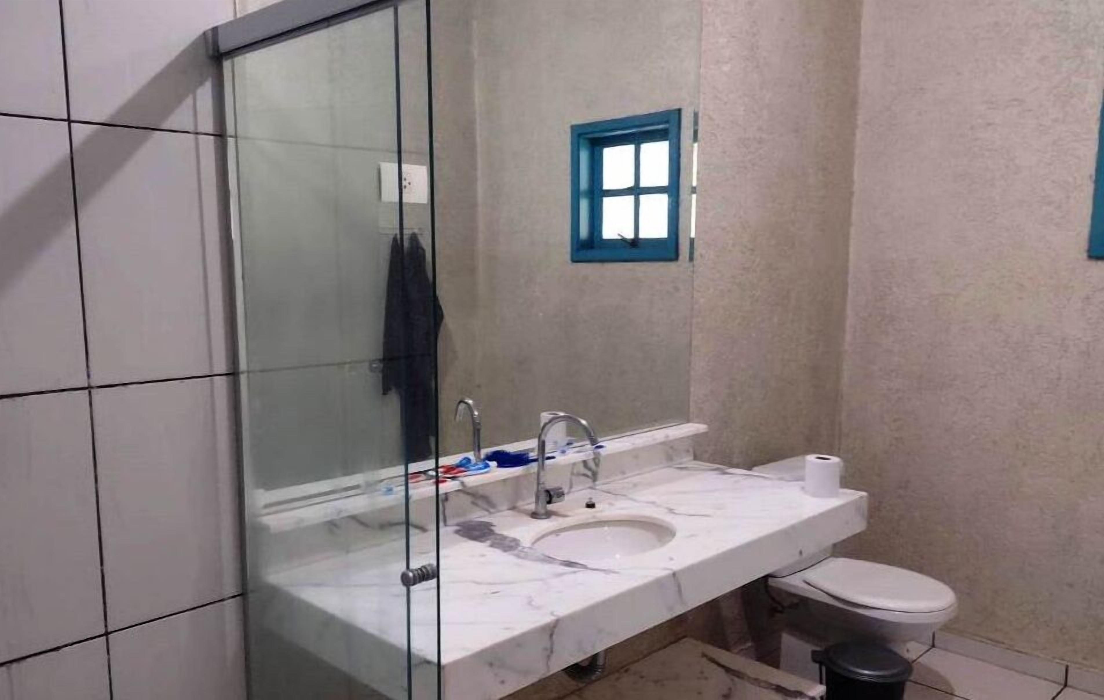 Casa de banho com lavatório de mármore branco, espelho, janela pequena e sanita.