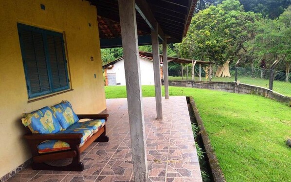 A covered patio area with a sofa and a stone-tiled floor. - Recanto das Corujas site, with a farmhouse style mansion (São João Novo)