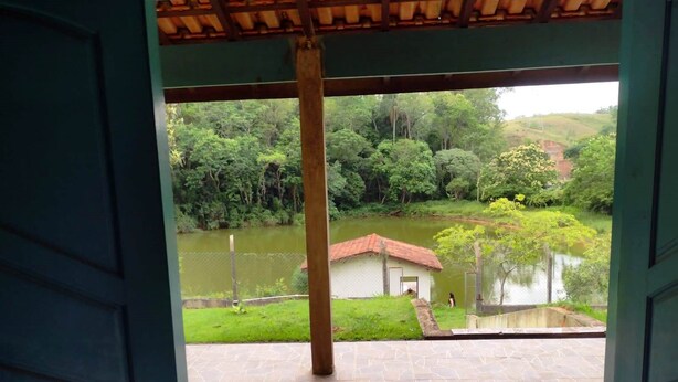 Vista da una stanza con pavimento piastrellato e soffitto in legno, su uno stagno con un piccolo edificio e vegetazione rigogliosa.