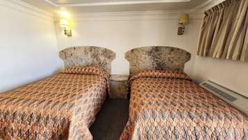 Ett hotellrum med två separata sängar, var och en med ett mönstrat överkast. Det finns väggmonterade lampor och en värmare på väggen.