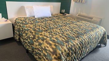 A neatly made bed with a patterned quilt, a white headboard, a bedside table with a phone, and a window with curtains.