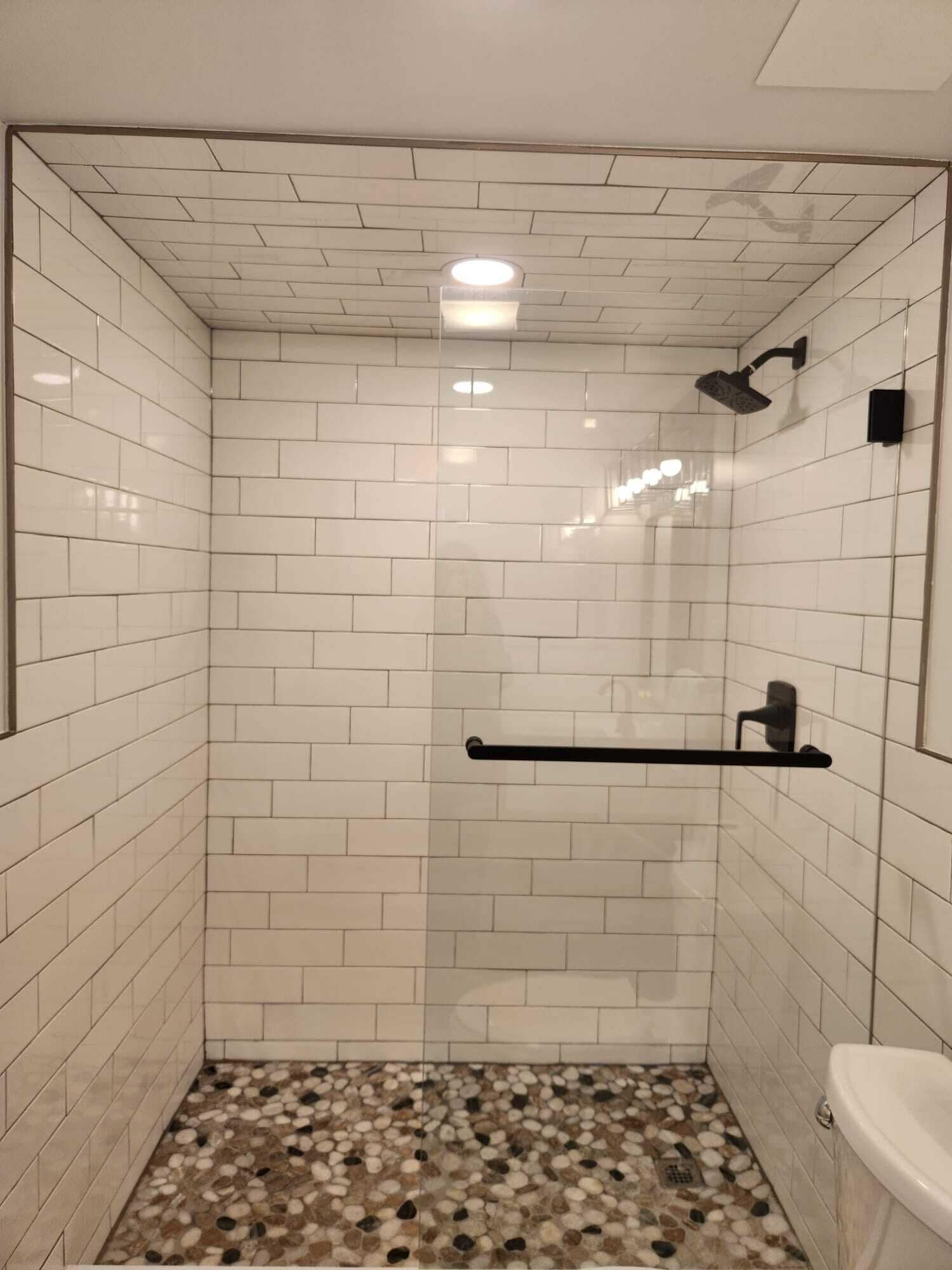 A small, tiled shower with a glass door, a black towel rack, and a white toilet.
