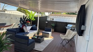 Una veranda coperta con mobili in vimini, un barbecue e piante in vaso.