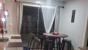 Un espace repas doté d’un comptoir en granit, de chaises en bois foncé, d’une table ronde et d’une cloison en verre agrémentée de rideaux légers.