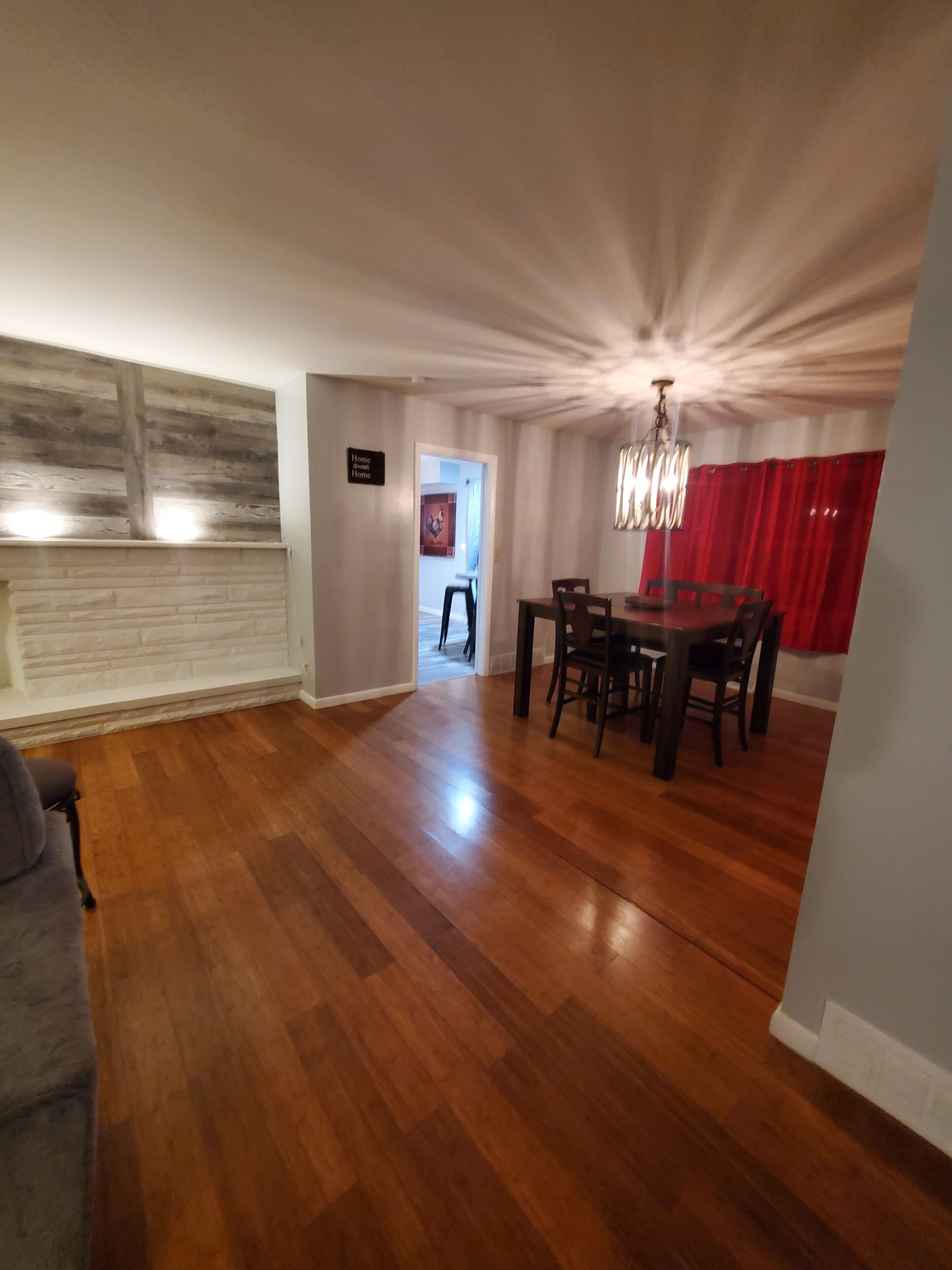A spacious living area with a wooden floor, a dining table with chairs, a chandelier, and a red curtain.