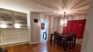 Un vaste espace de vie doté d’un plancher en bois, d’une table à manger avec des chaises, d’un lustre et d’un rideau rouge.