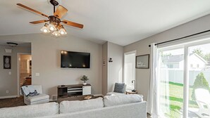 Ein Wohnzimmer mit Deckenventilator, Flachbildfernseher, Sofa, Couchtisch und einer Glastür, die in einen Hinterhof führt.