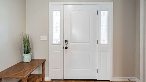 Eine weiße Tür mit Schlüsselloch und Knauf, begleitet von zwei Fensterfeldern mit Zierverzierungen.