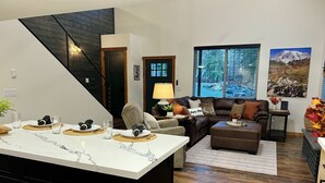 Een moderne woonkamer met een bruine leren bank, een eethoek met een witte marmeren tafel en een trap met donker houten lambrisering.