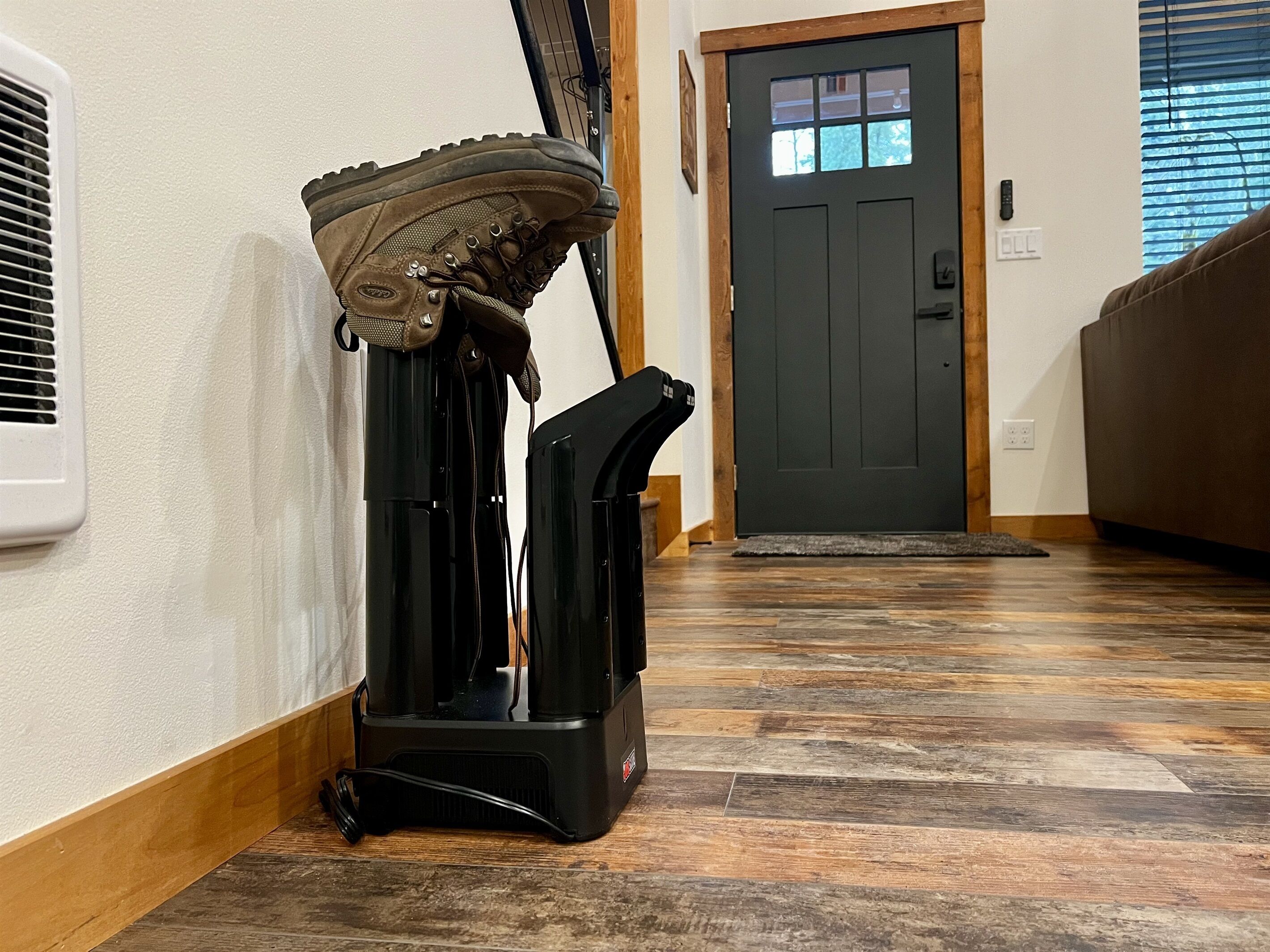 A vacuum cleaner in a hallway with a wooden floor, a door, and a vent on the wall.