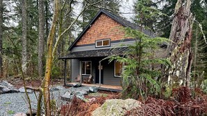 Een chalet met een donkere gevel, een schuin dak en een veranda met twee stoelen.